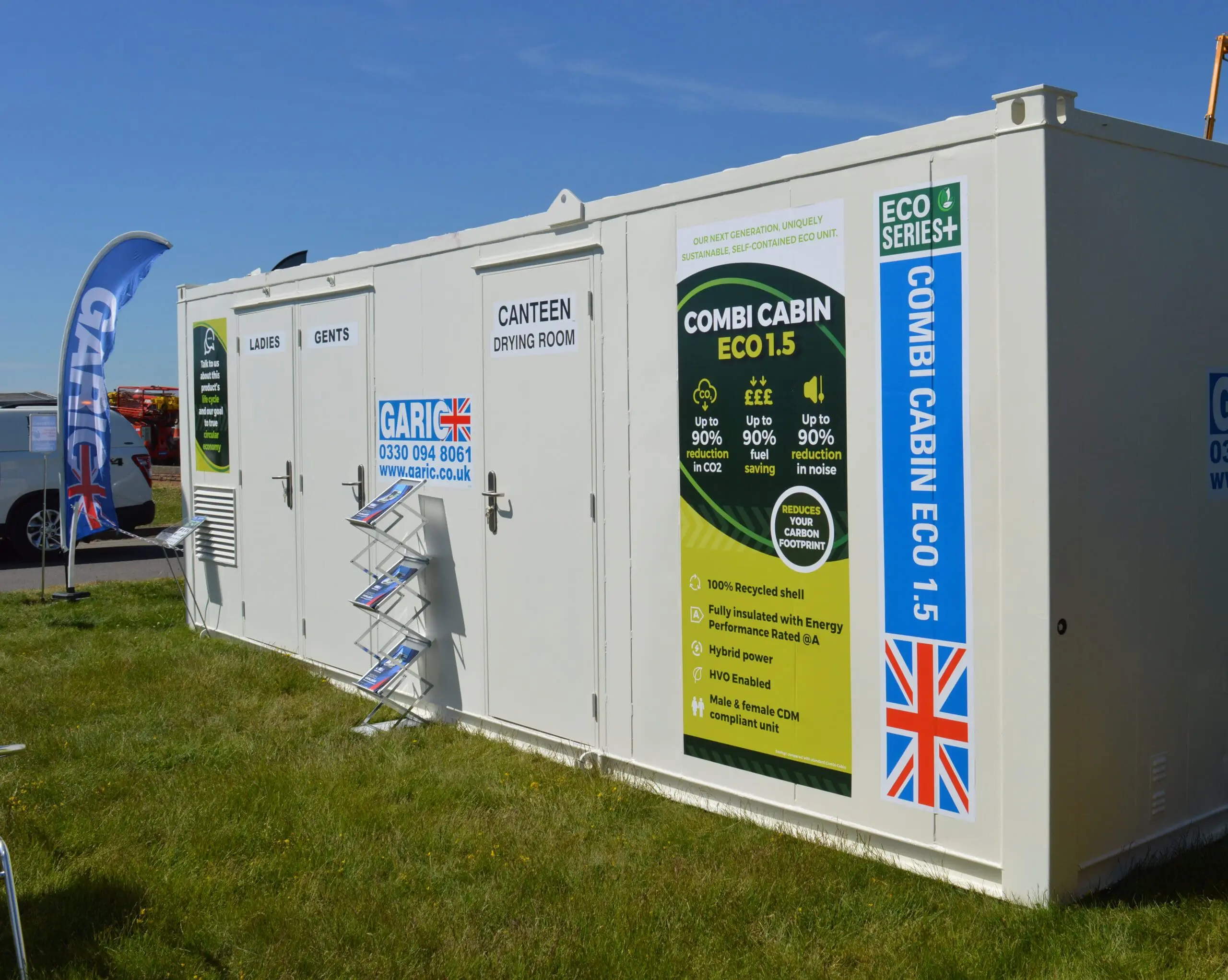 White portable cabin with UK flag, labeled for canteen, ladies, and gents, on a grassy outdoor area.