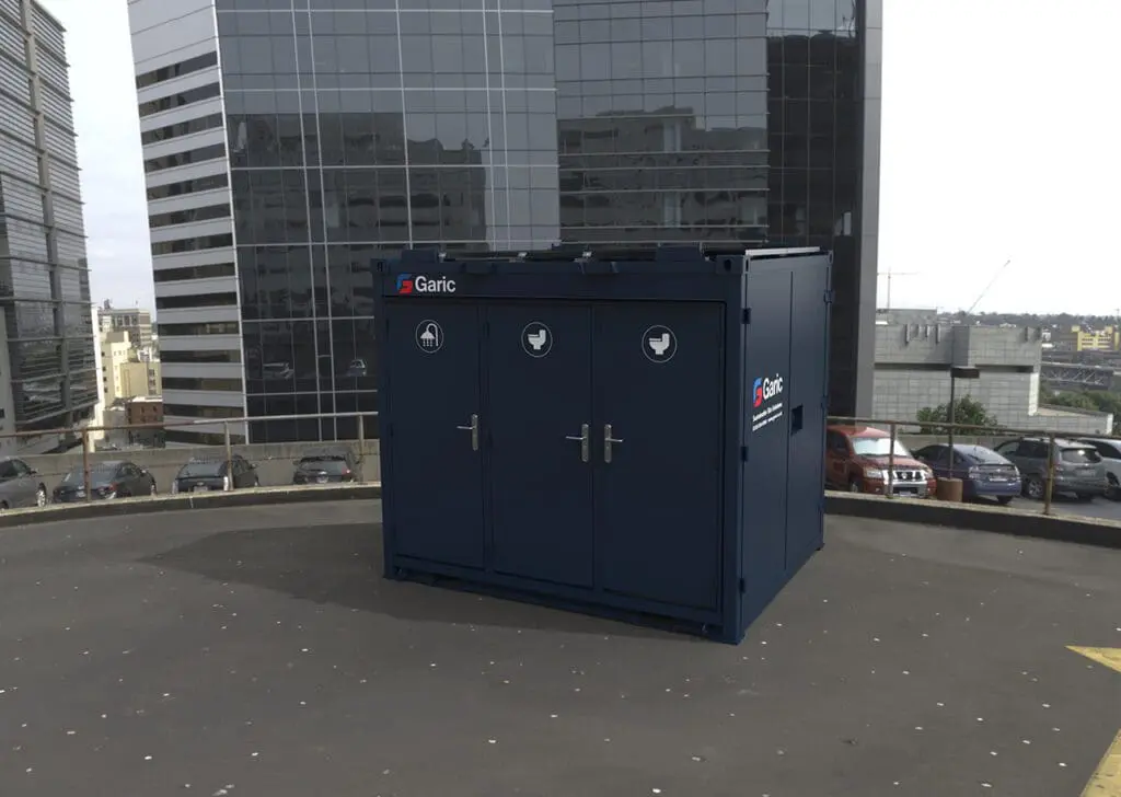 A 1+1 Toilet Block 10 unit sits on a rooftop, surrounded by tall office buildings and parked cars.