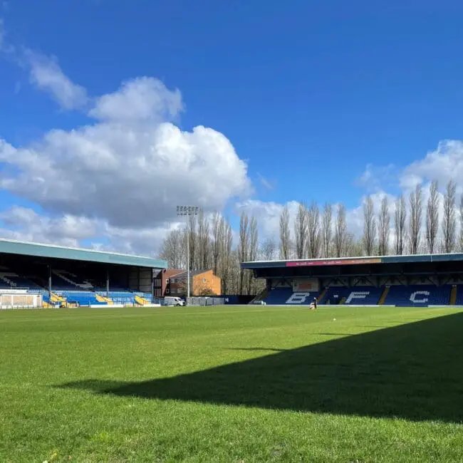 Empty football stadium with green grass, blue seats, and clear sky with fluffy clouds.