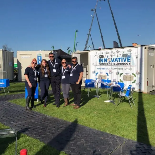 Five people pose together outside at an event next to a booth with a sign reading Innovative Power in Technology.