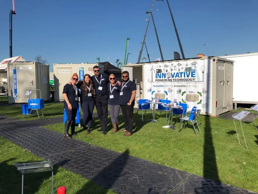 Five people pose together outside at an event next to a booth with a sign reading Innovative Power in Technology.