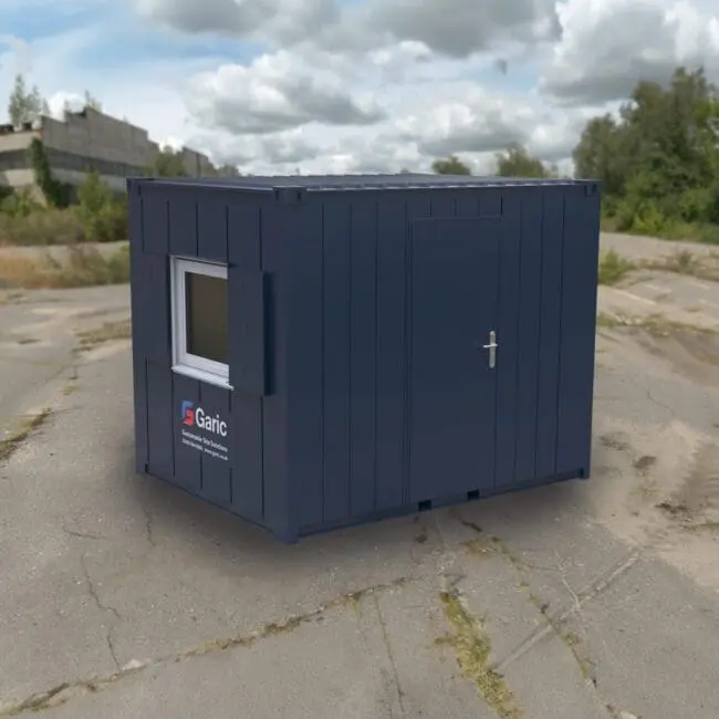 The Accommodation 10 is a small blue portable cabin with a window and door, situated on cracked pavement outdoors.