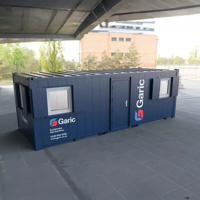 Accommodation Eco 24 portable cabin with windows and door, placed outdoors beneath a large concrete structure.