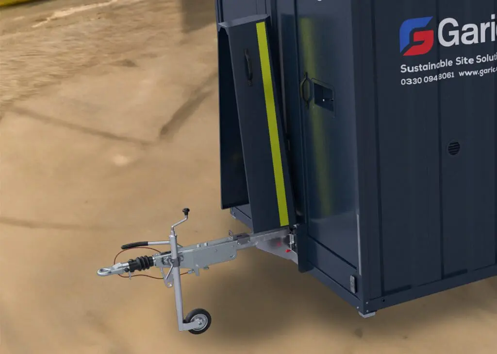 Close-up of an Armadillo 18 Eco portable site cabin with a tow hitch, parked on a wet, muddy surface.