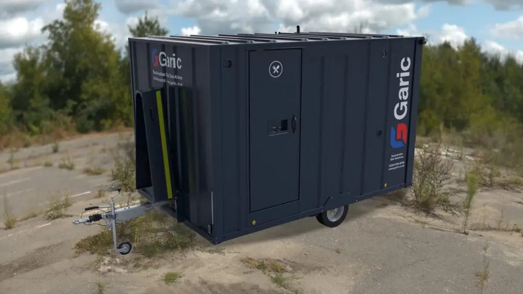 Dark blue Armadillo 12 mobile restroom trailer with Garic branding, parked on a cracked outdoor surface with weeds.