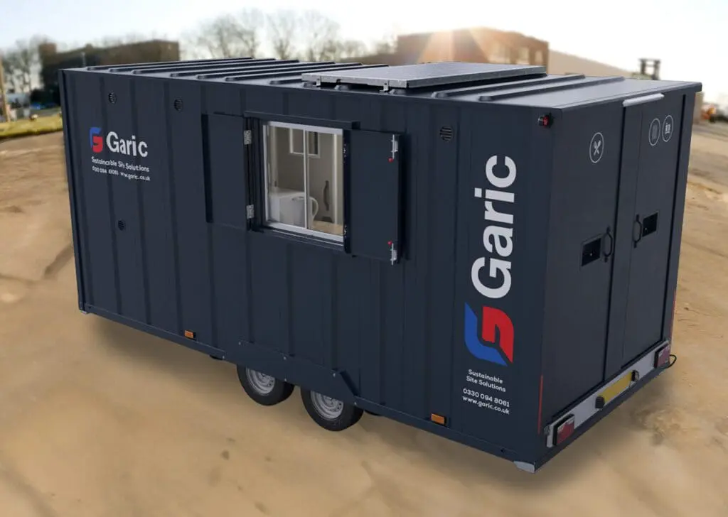 The Armadillo 18 Eco, a dark blue mobile site cabin with window, doors, and wheels, is parked on a construction site.