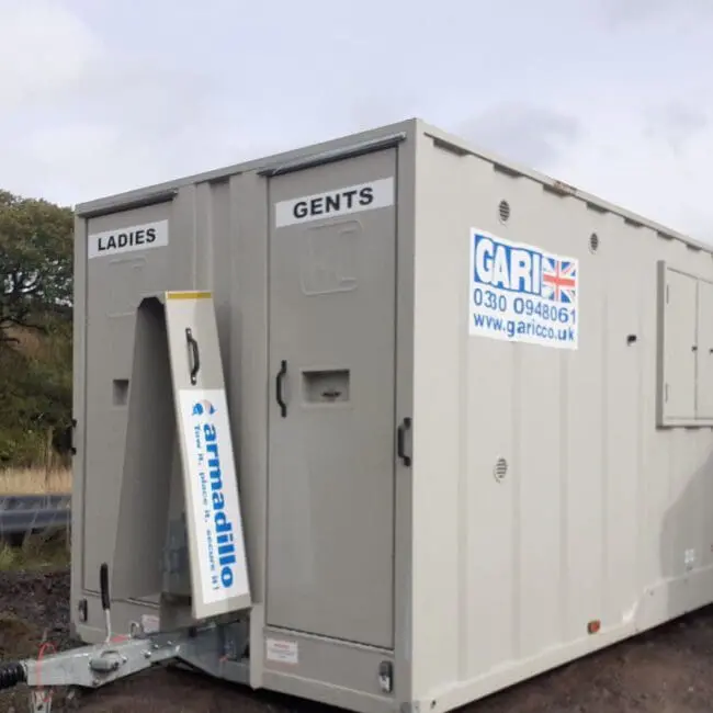 Mobile restroom trailer labeled Ladies and Gents parked outdoors on a grassy area.