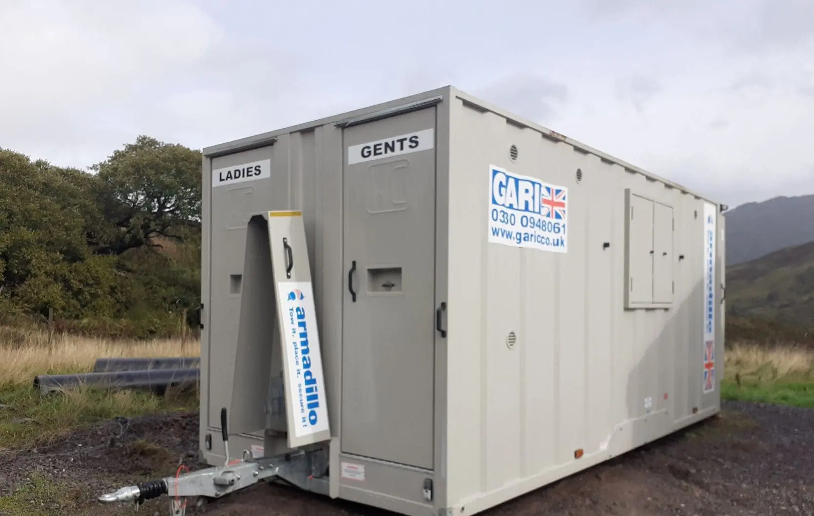 Mobile restroom trailer labeled Ladies and Gents parked outdoors on a grassy area.