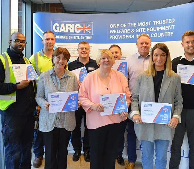 Nine people holding certificates, standing in front of a GARIC promotional banner in an indoor setting.