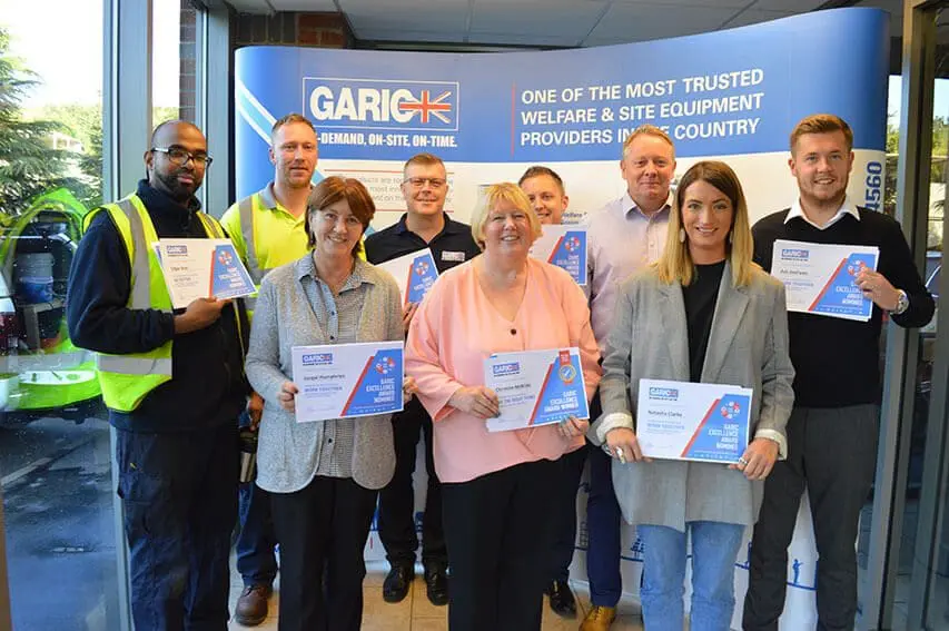 Nine people holding certificates, standing in front of a GARIC promotional banner in an indoor setting.