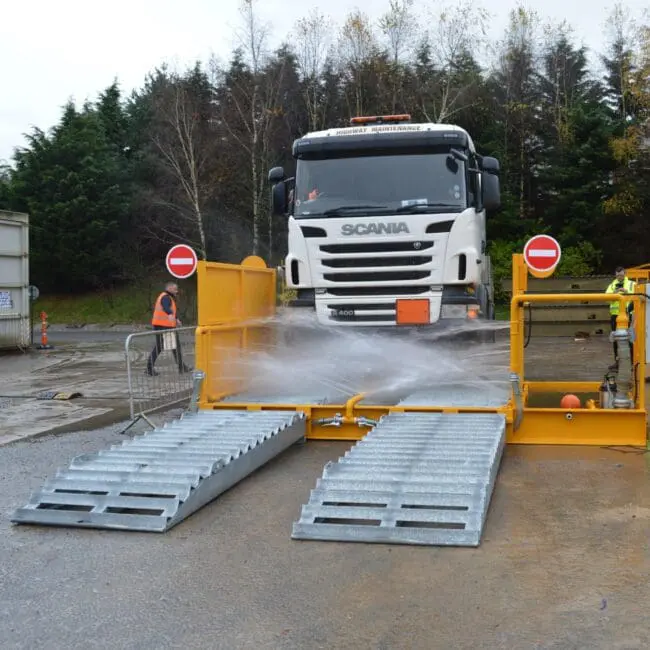 A truck is being washed at a vehicle wash station with water spraying from below.