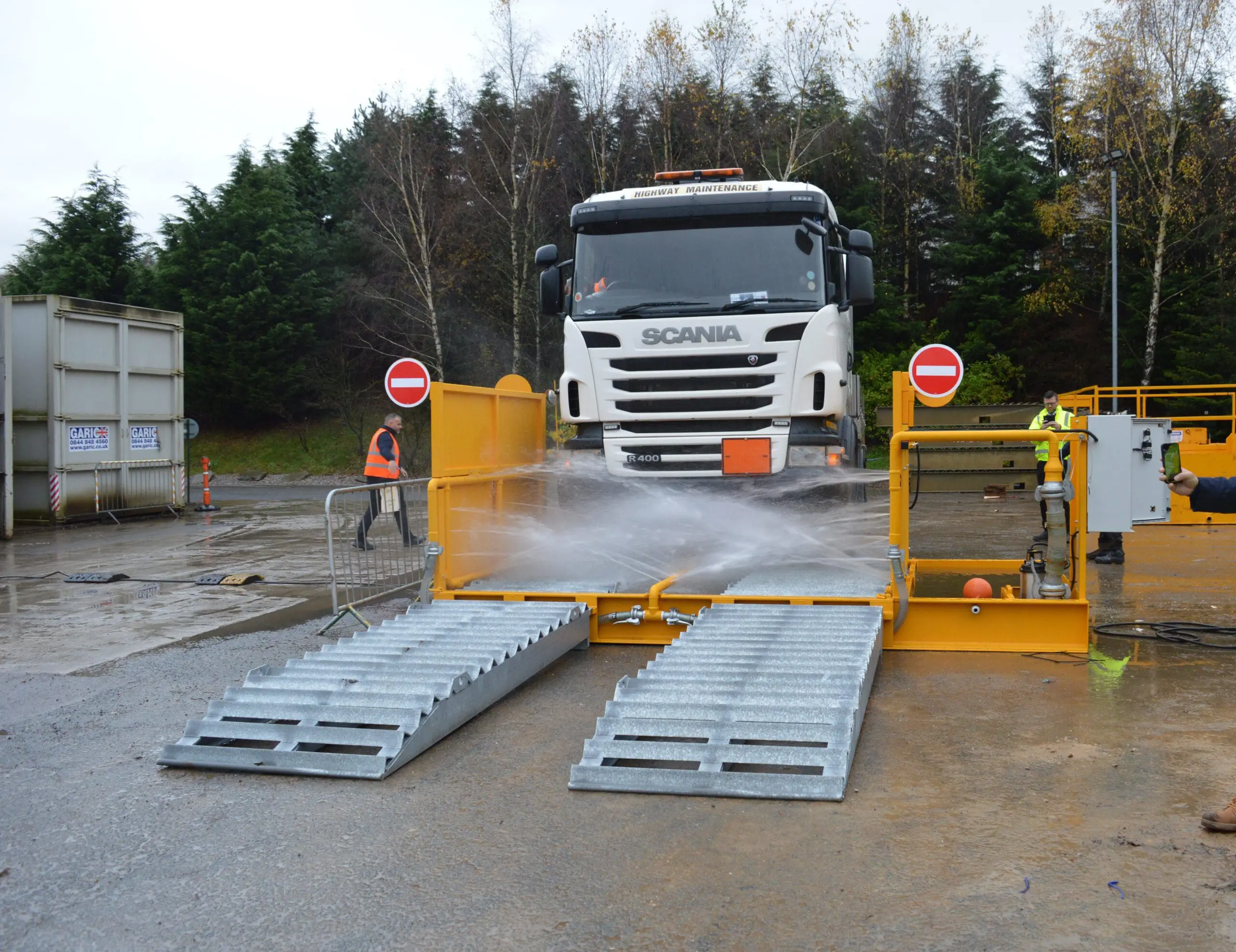 A truck is being washed at a vehicle wash station with water spraying from below.