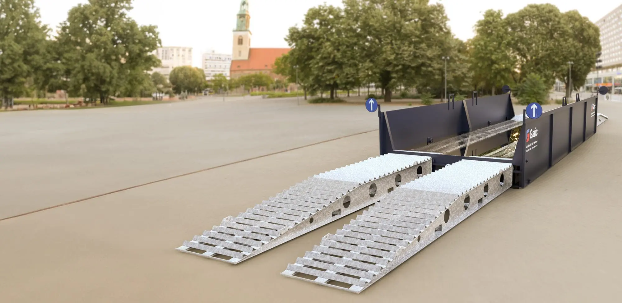 An Enviro Bath 12 portable metal bridge with ramps is set up on an empty, paved outdoor area with trees in the background.