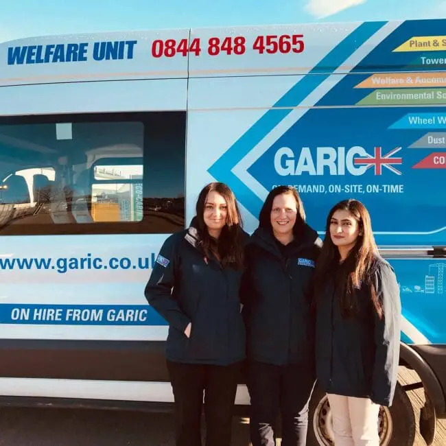 Three women in jackets stand in front of a Garic welfare unit van with blue and yellow branding.