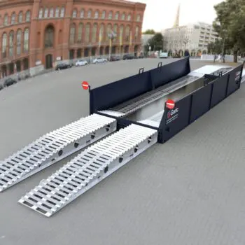 The Enviro Bath 12 portable metal vehicle ramp is set up outdoors on a paved area, with buildings and trees in the background.