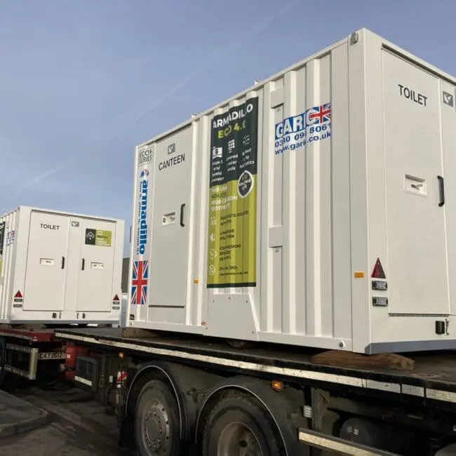 Two white portable units labeled Toilet and Canteen on a flatbed truck, outdoors on a clear day.