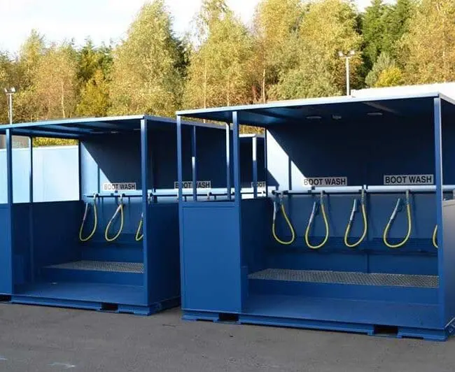 Two blue outdoor boot wash stations with hoses, labeled BOOT WASH, on a paved area near trees.