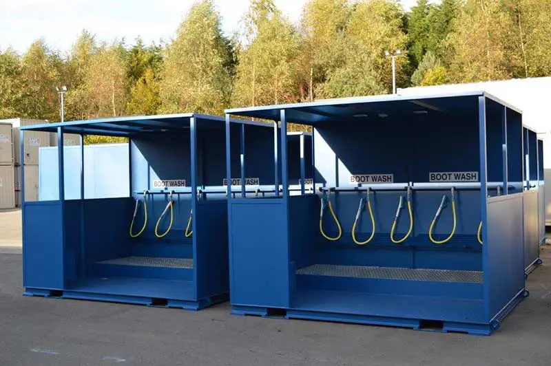 Two blue outdoor boot wash stations with hoses, labeled BOOT WASH, on a paved area near trees.