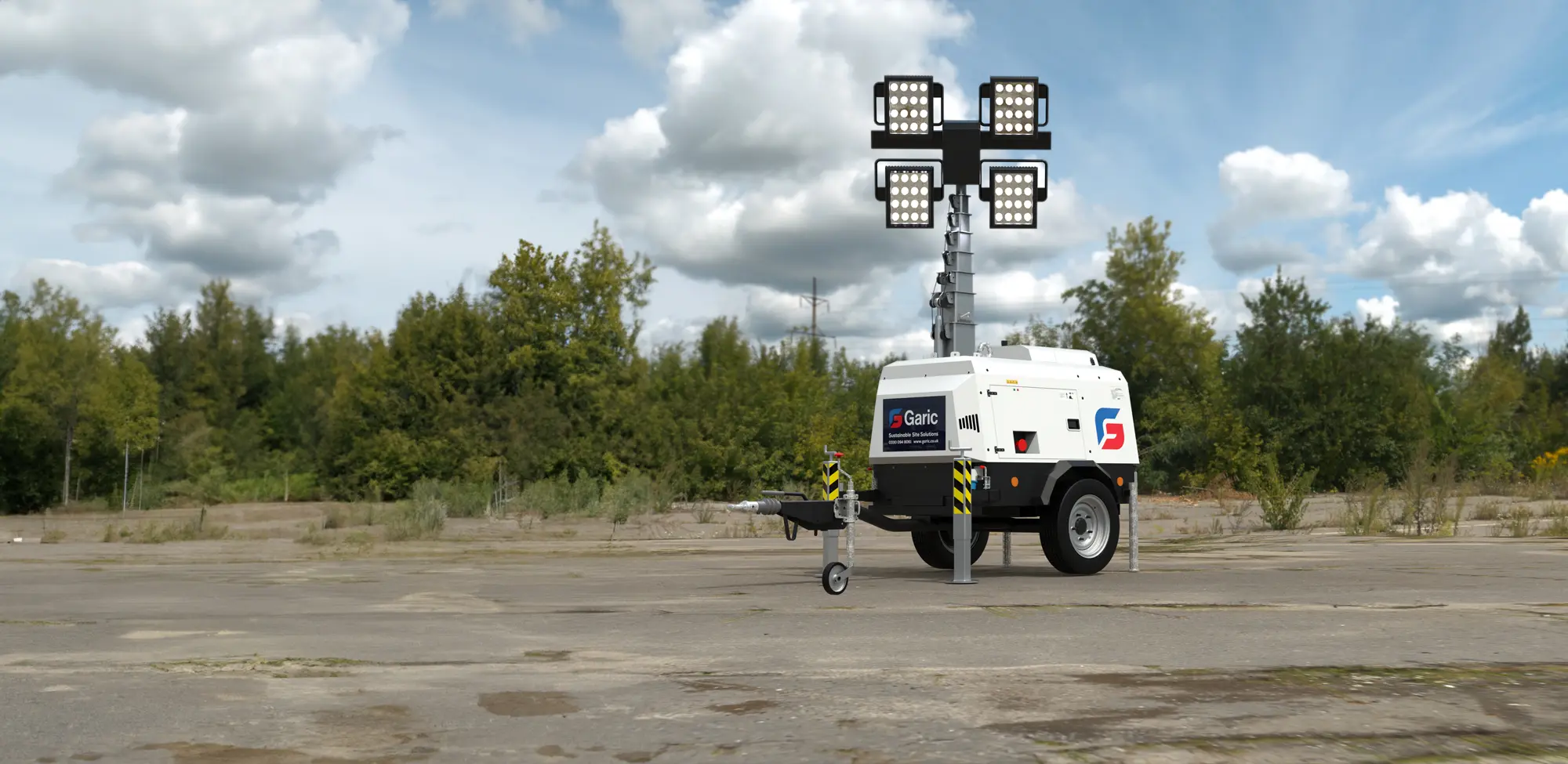 The Hybrid Tower Light, equipped with four floodlights, stands on a paved area surrounded by trees and clouds.