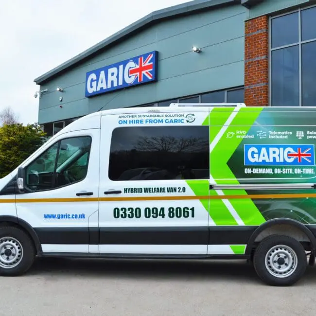 White Garic hybrid welfare van parked outside a modern building with large windows and a Garic sign.