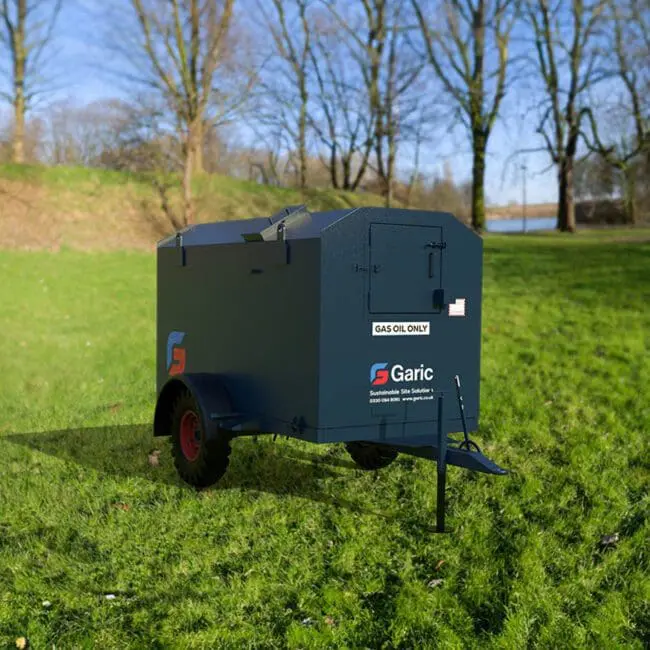 A dark blue Mobile Fuel Tanks trailer marked Garic sits on green grass with trees in the background.