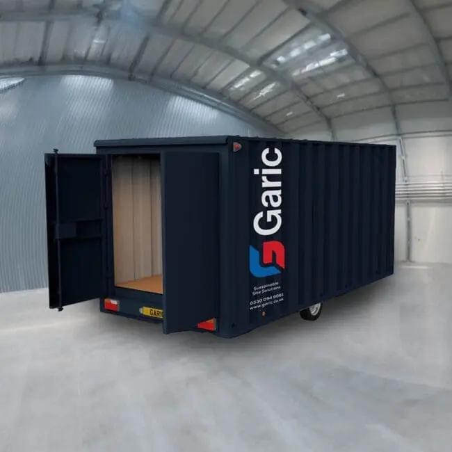 A Mobile Store 12 in dark blue with open doors is positioned inside a large, empty warehouse with a curved roof.