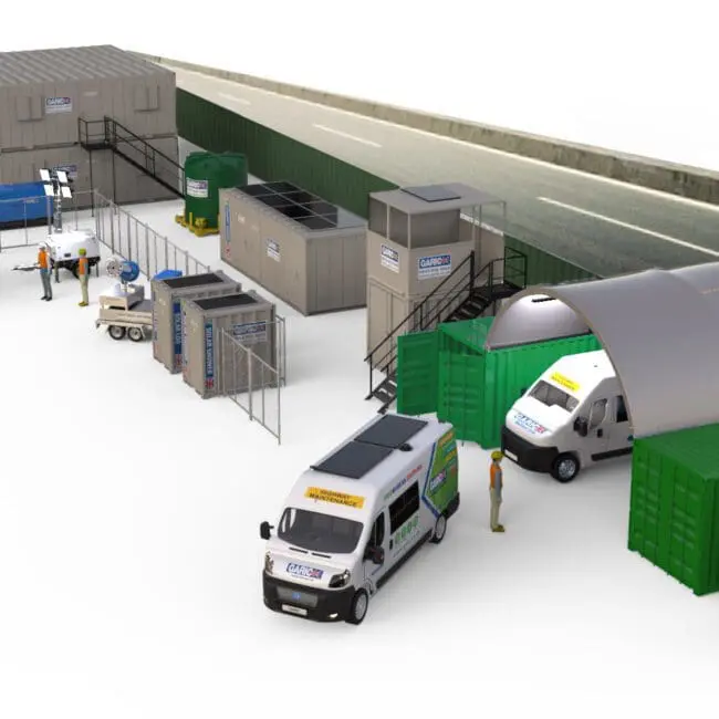 A row of portable buildings, vehicles, solar panels, and workers set up along a road.