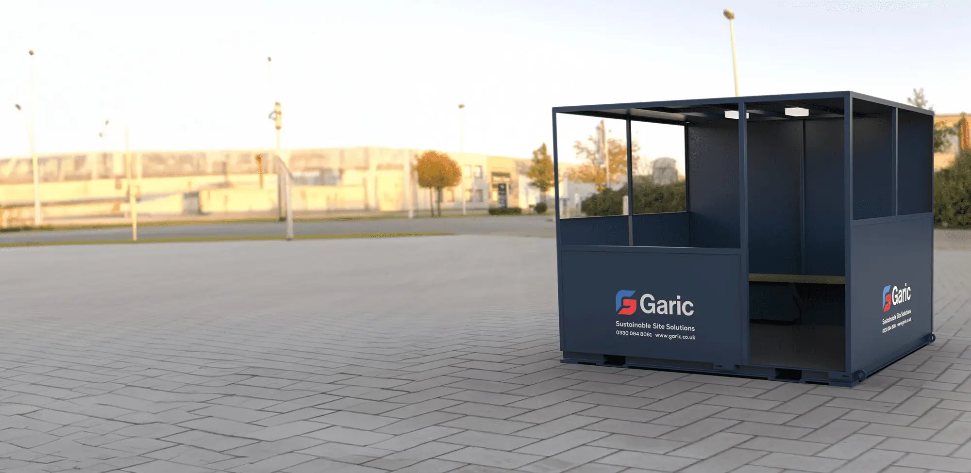 A blue Shelter 10 smoking shelter with benches stands in an empty paved outdoor area.