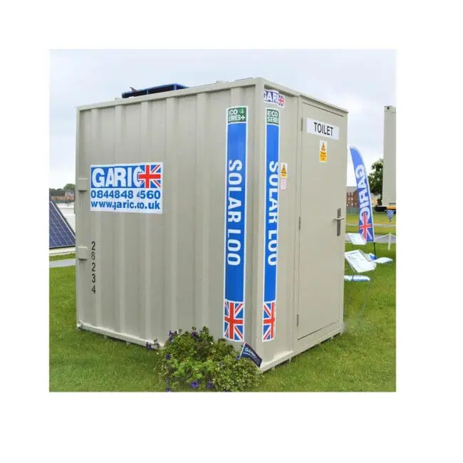 A portable toilet labeled SOLAR LOO with UK flags and a Garic company logo, on a grassy area.