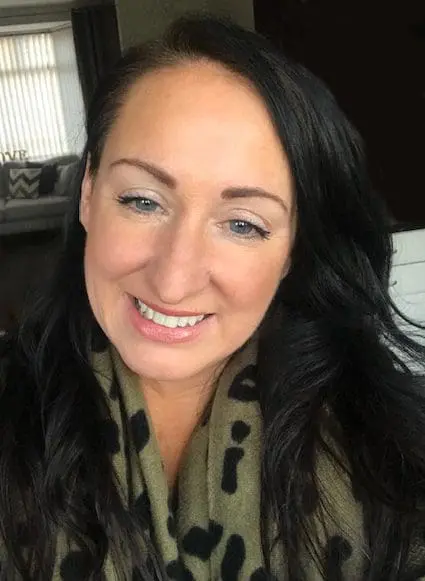 A woman with long dark hair smiles at the camera, wearing a green scarf with black spots.