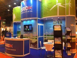 Bright exhibition booth with brochures, a TV screen, chairs, and wind turbine graphics on the walls.