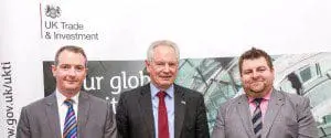 Three men in suits standing in front of a UK Trade & Investment banner, smiling at the camera.