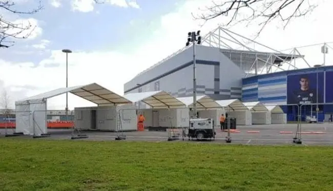White temporary tents set up outside a modern building, with workers and equipment visible nearby.