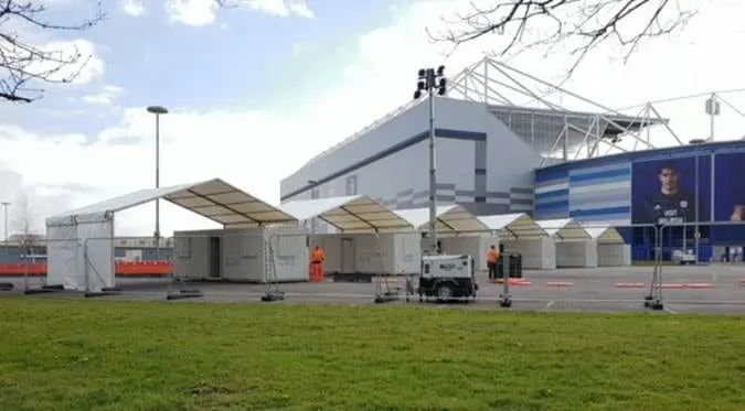 White temporary tents set up outside a modern building, with workers and equipment visible nearby.