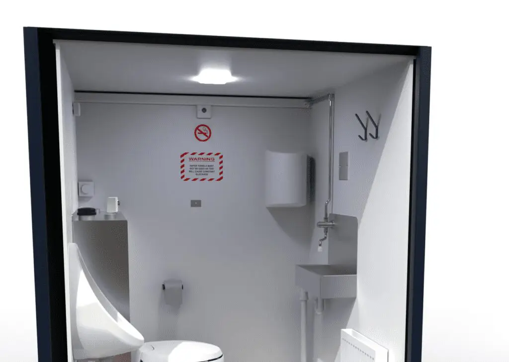 The Solar Loo 8 features a compact bathroom equipped with a toilet, urinal, sink, hooks, warning sign, and a no smoking sign on the wall.