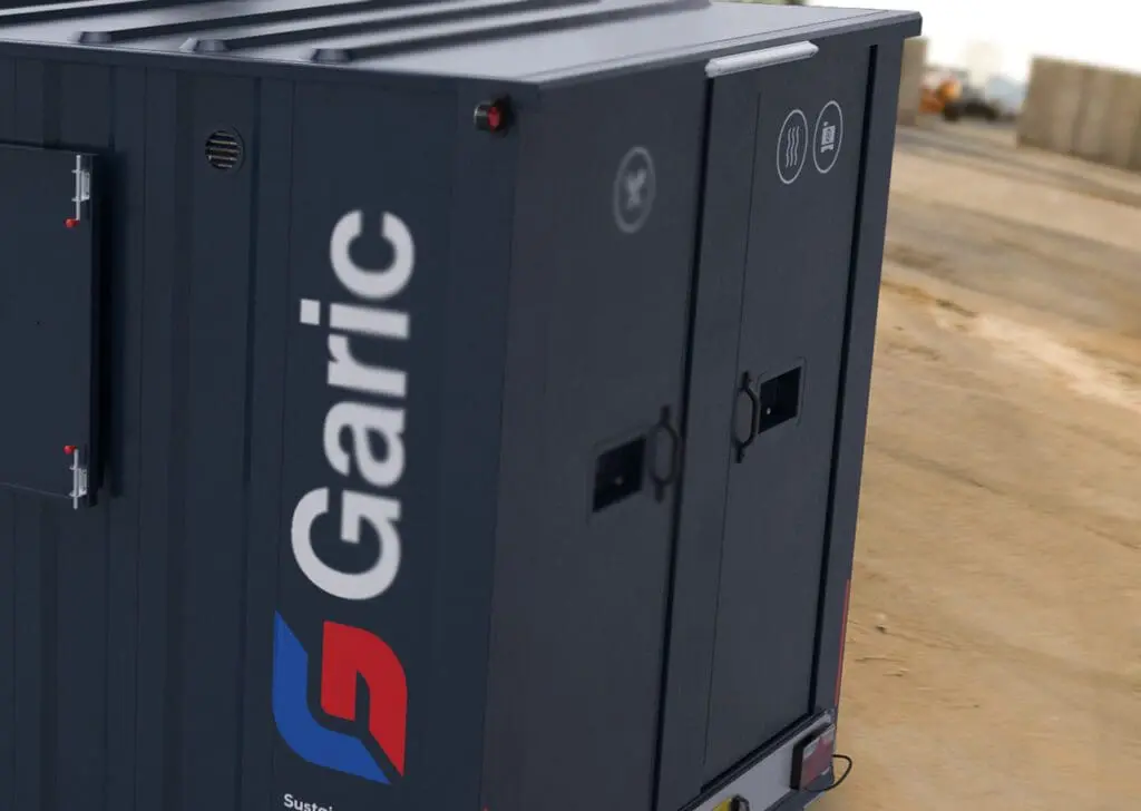 Armadillo 18 Eco: Dark portable unit with Garic branding, closed double doors, and safety icons, situated on a construction site.