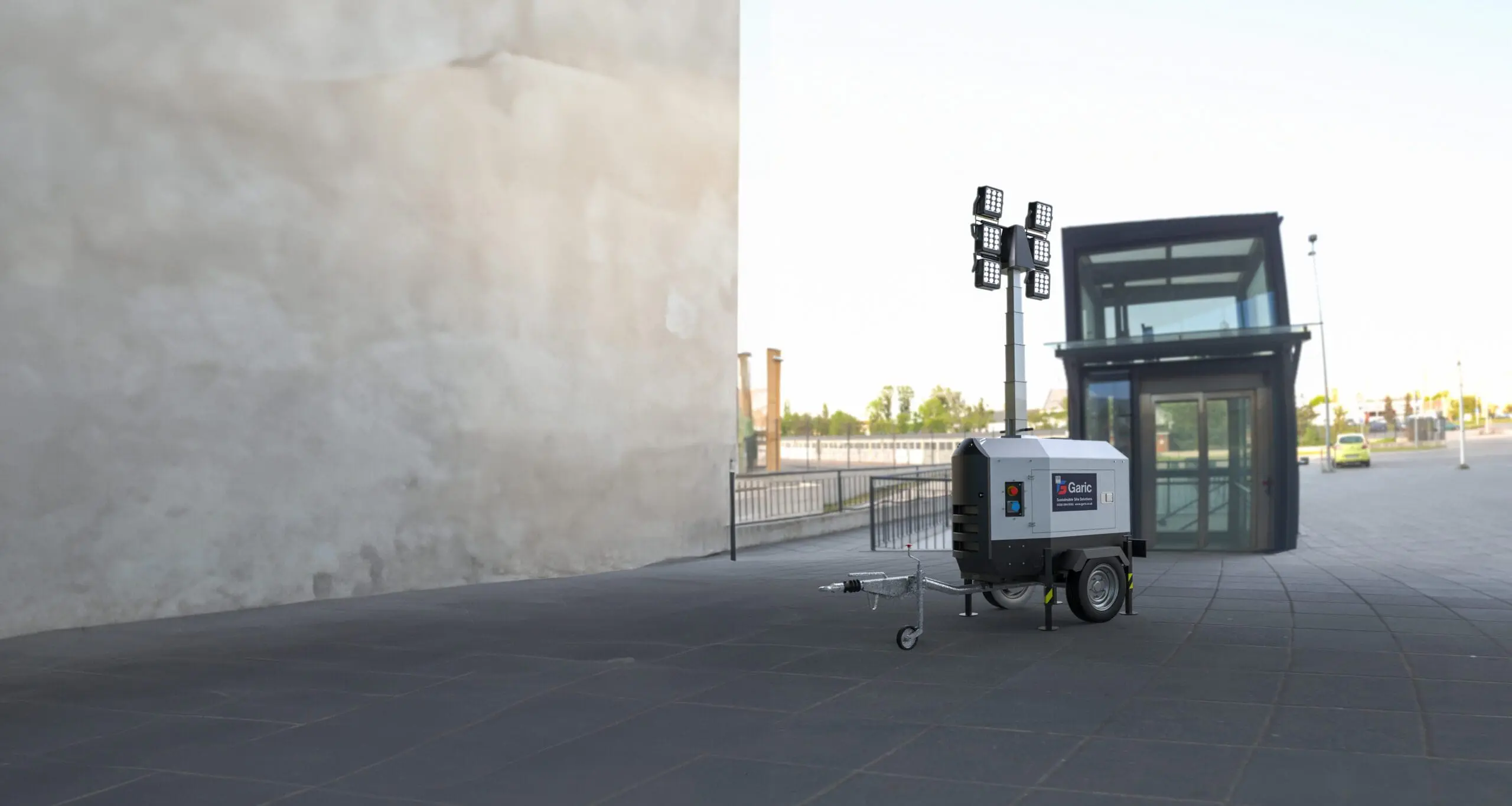 An Eco Tower Light stands on a paved area near a modern glass building and a large wall.