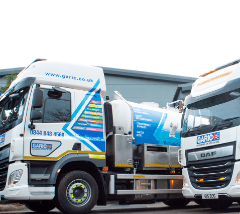 Two Garic-branded trucks parked side by side in front of a modern industrial building.