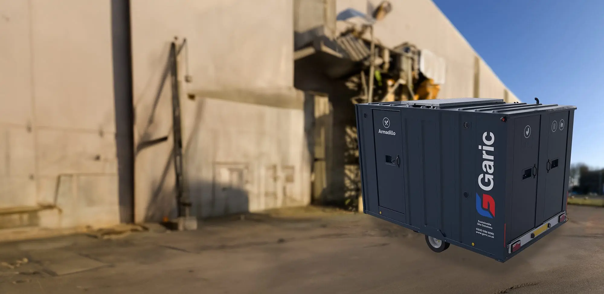An Armadillo 12 Eco mobile unit in dark gray is parked outside a weathered industrial building on a sunny day.