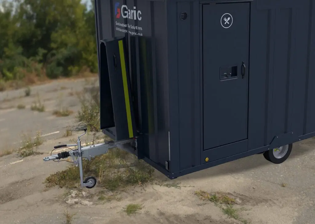 A black Armadillo 12 Eco mobile trailer with Garic branding is parked on a rough outdoor surface near greenery.