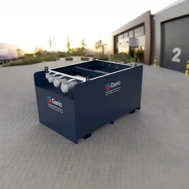 A blue Settlement Tank 4500 is placed on a paved area outside an industrial building with large roll-up doors.