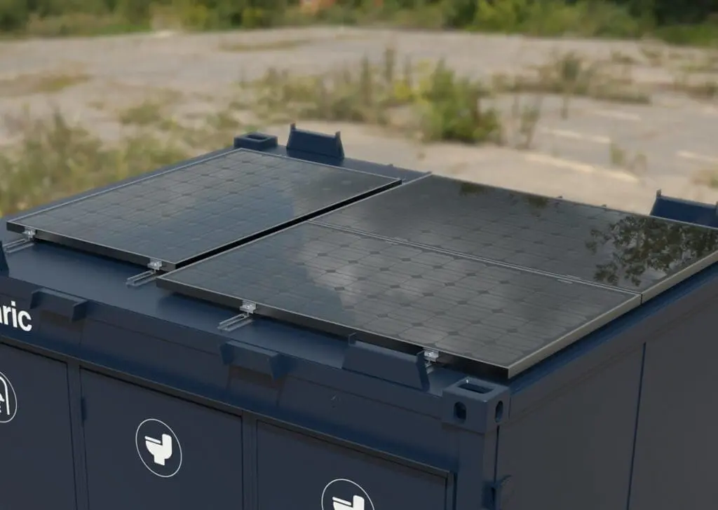 Close-up of the 1+1 Toilet Block 10 with solar panels mounted on top of a blue unit, set outdoors with greenery in the background.