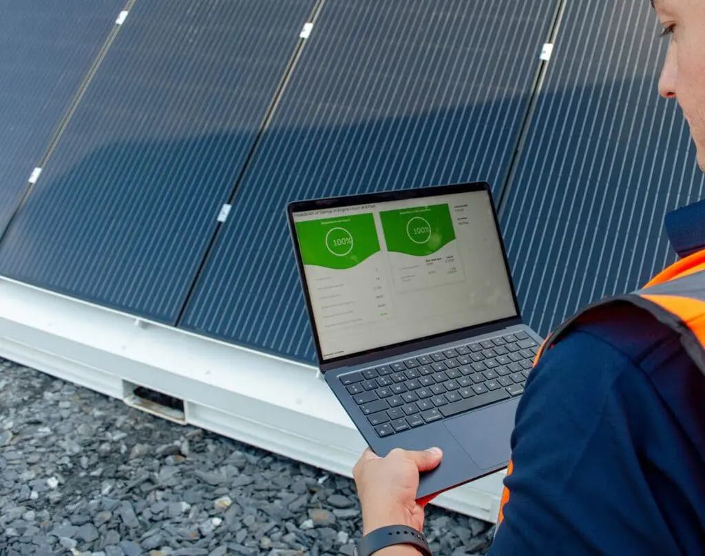 A person stands in front of solar panels holding a laptop that displays energy data, showcasing the Welfare Van Eco+.