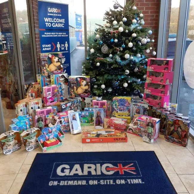 Christmas tree with ornaments surrounded by various donated toys inside an office lobby with Garic branding.
