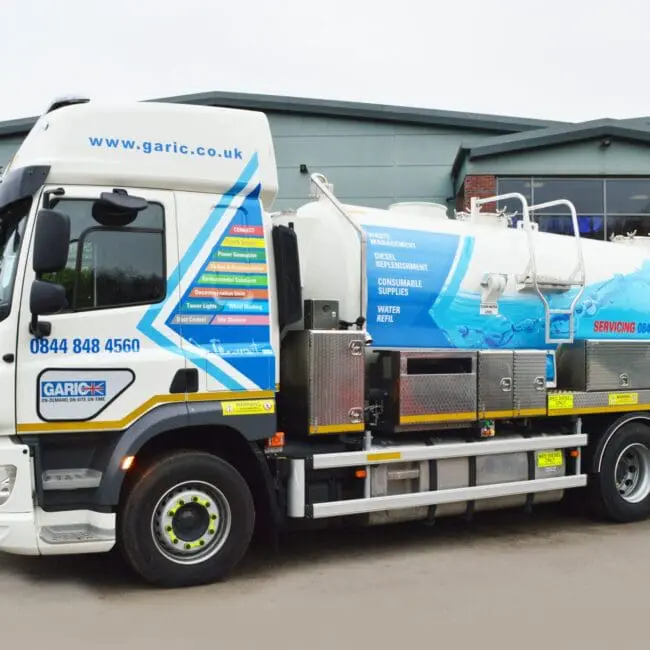 A large vacuum tanker truck with company branding parked outside an industrial building.