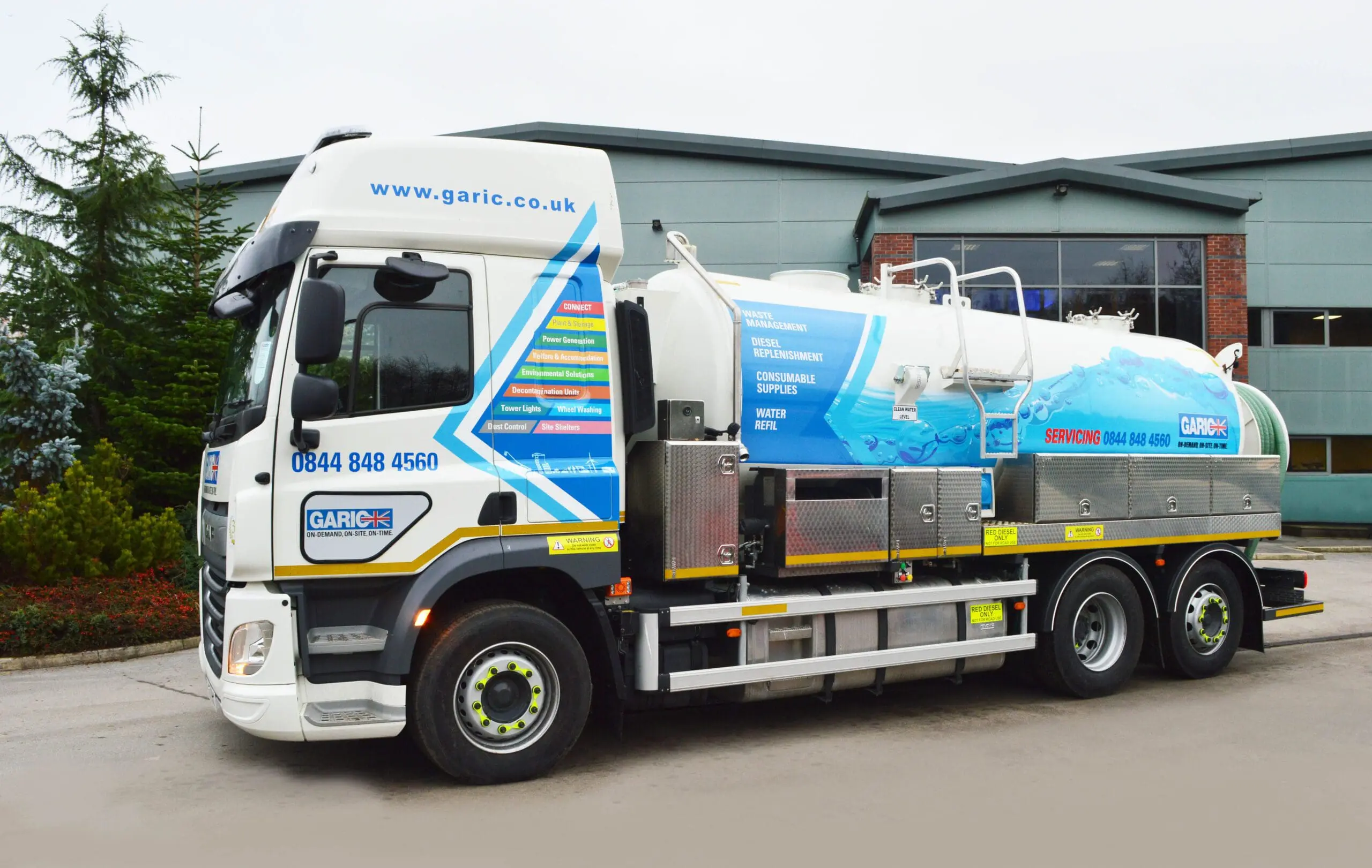 A large vacuum tanker truck with company branding parked outside an industrial building.