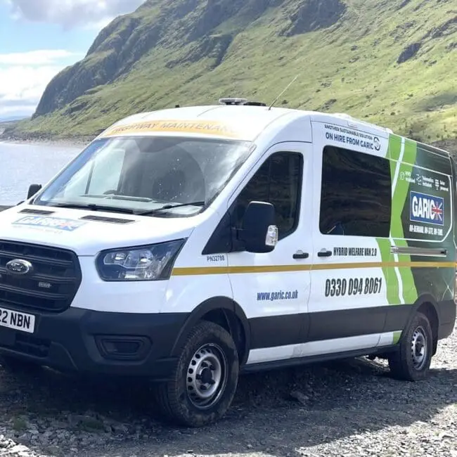 White and green GAP Group van parked on a rocky path in a scenic, mountainous landscape.