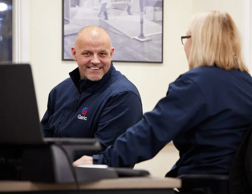 Two people in uniforms smiling and talking at an office desk with a computer.
