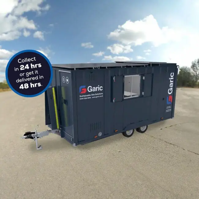 A dark blue Armadillo 18 Eco+ portable unit on wheels in an empty outdoor area, displaying a sign about collection and delivery times.