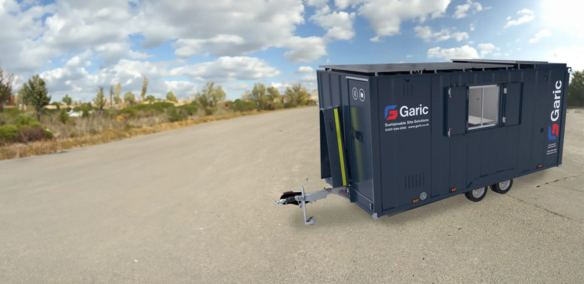 A dark grey Armadillo 18 Eco+ portable unit on wheels is parked on a wide, empty paved area beneath a partly cloudy sky.